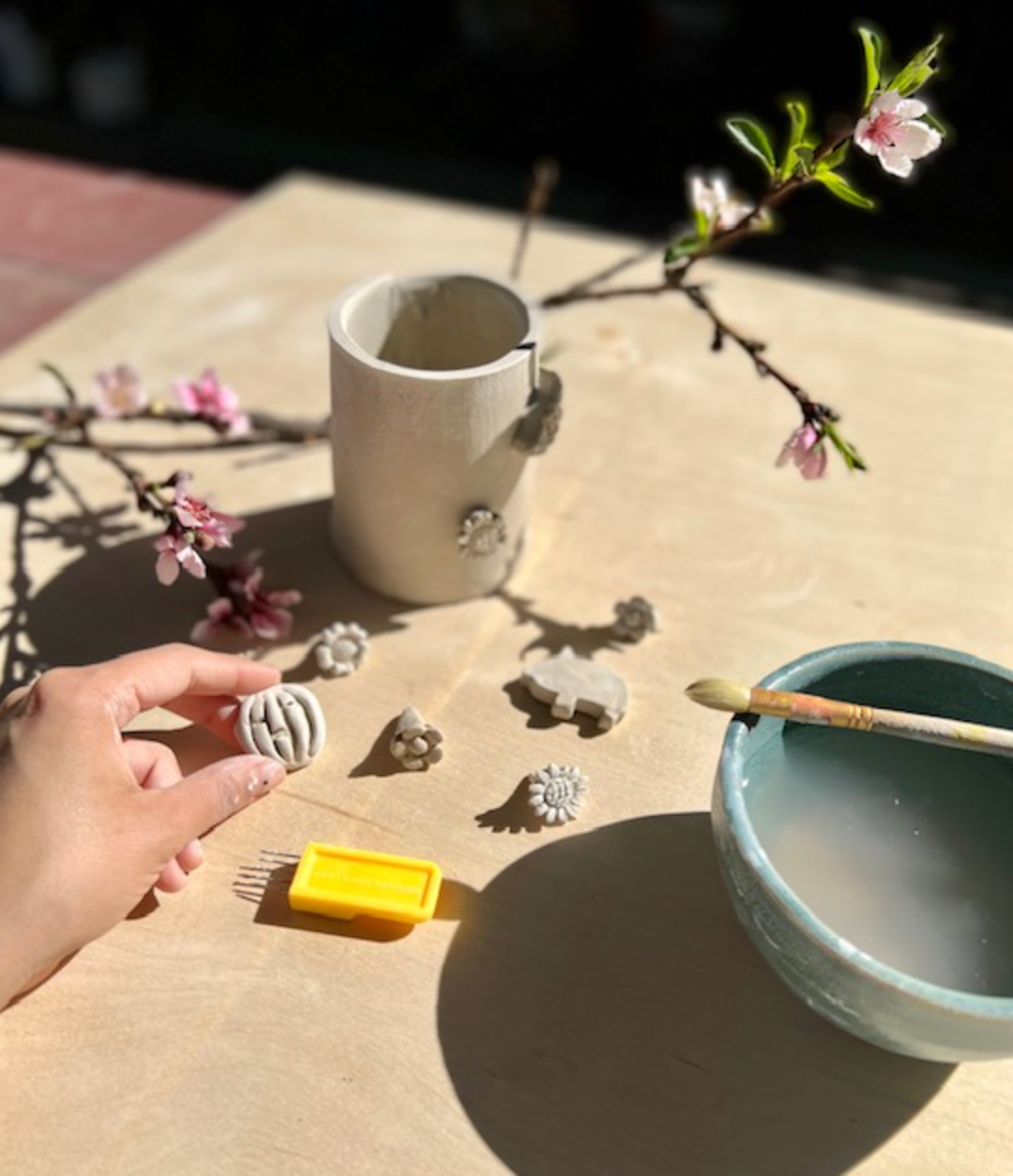 Image of a hand working with ceramics to create clay decorations for a small pot in the background.