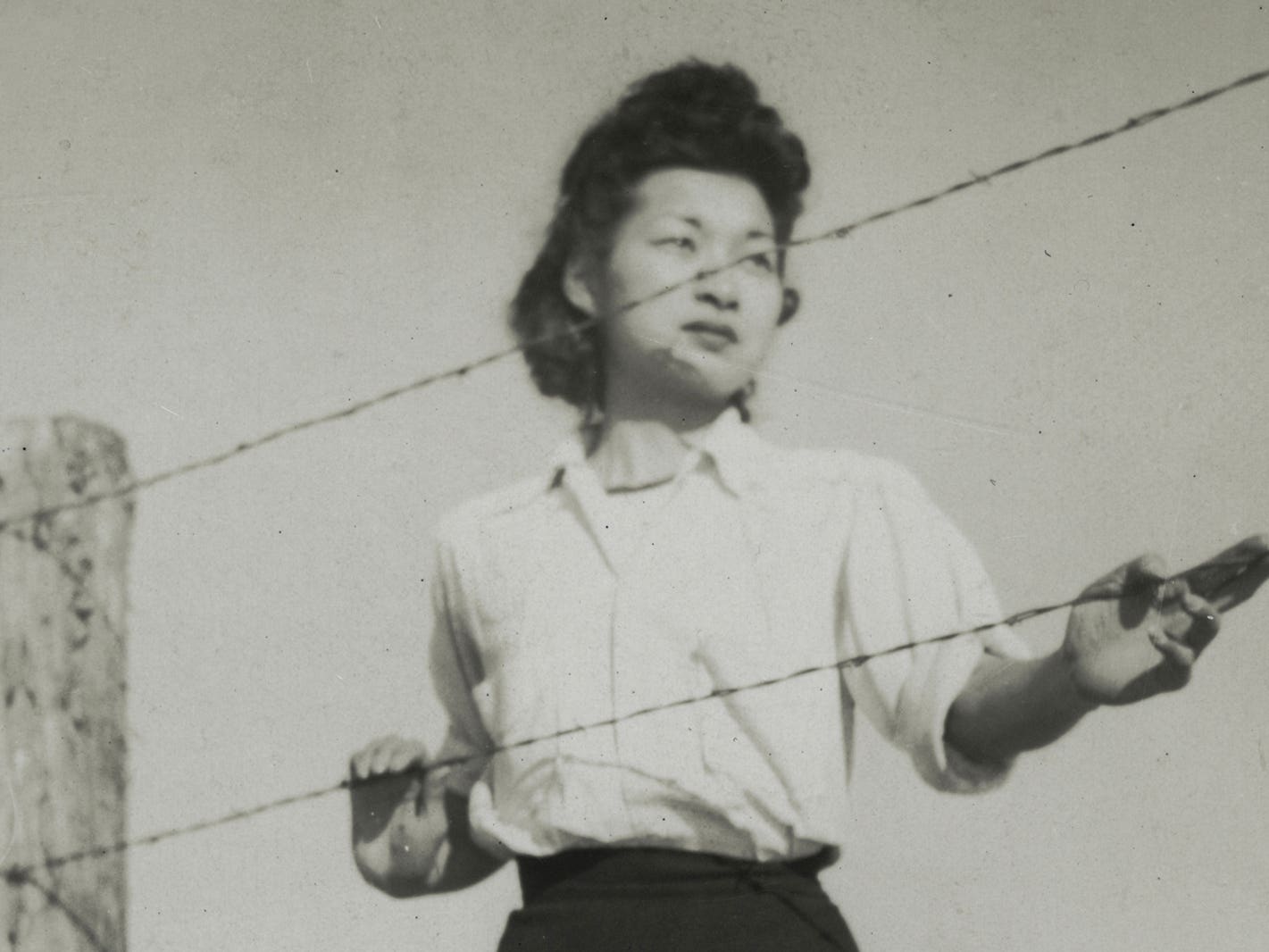 a young woman standing by the barbed wire fence of the Manzanar concentration camp. Anonymous. Gift of Myrtle Joyce Barley Ward, JANM. 2003.12.14.