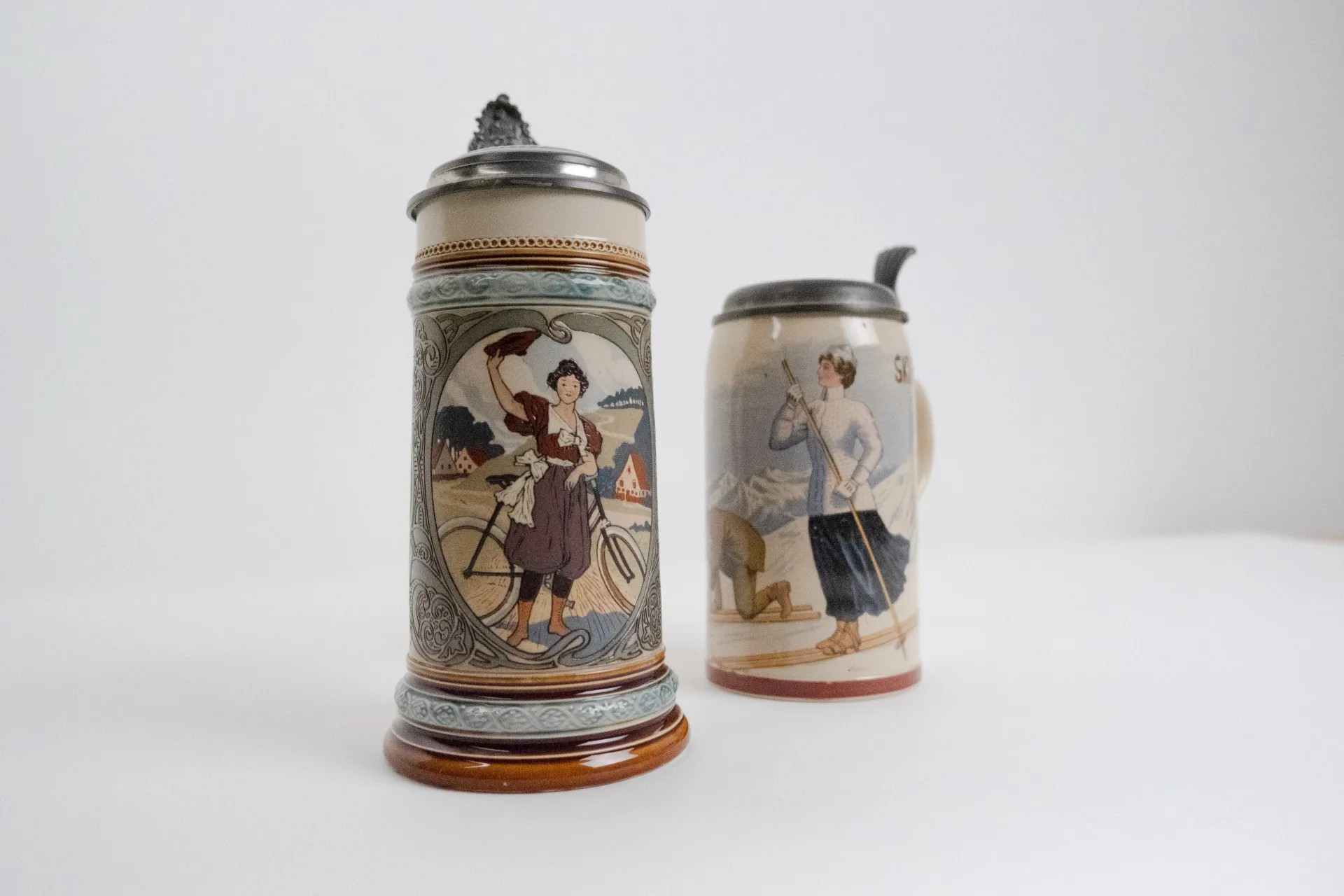 Villeroy and Boch. Girl Holding Safety Bicycle. Stein, etched, inlay. 1900. Collection of the American Museum of Ceramic Art; gift of Bob and Colette Wilson. (foreground)  Villeroy and Boch. Woman Skiing. Stein, print-under-glaze. 1911. Collection of the American Museum of Ceramic Art; gift of Bob and Colette Wilson. (background)