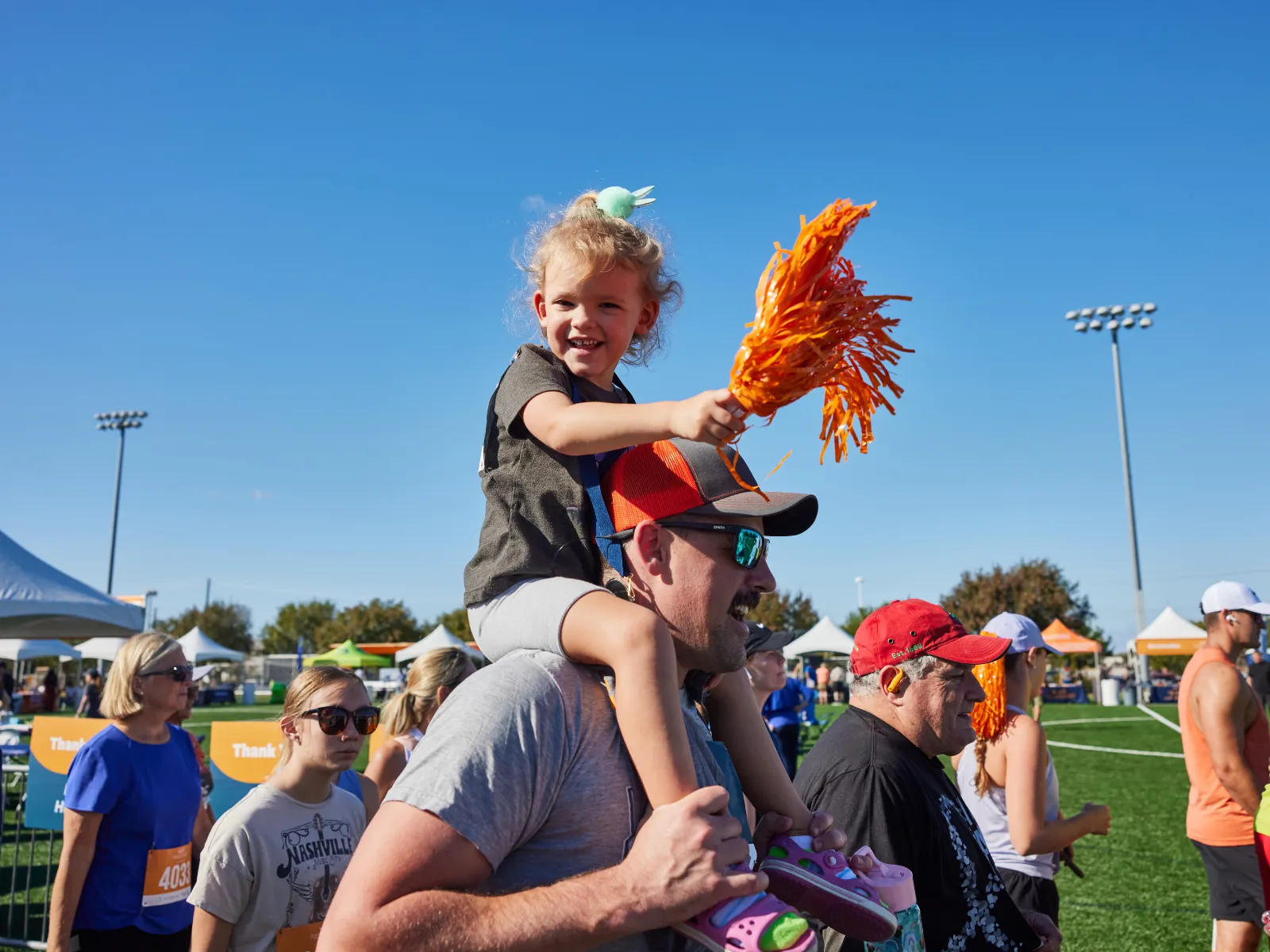 A young child sits on her father's shoulders, cheering for runners at the Michael J. Fox Foundation Run/Walk event. 